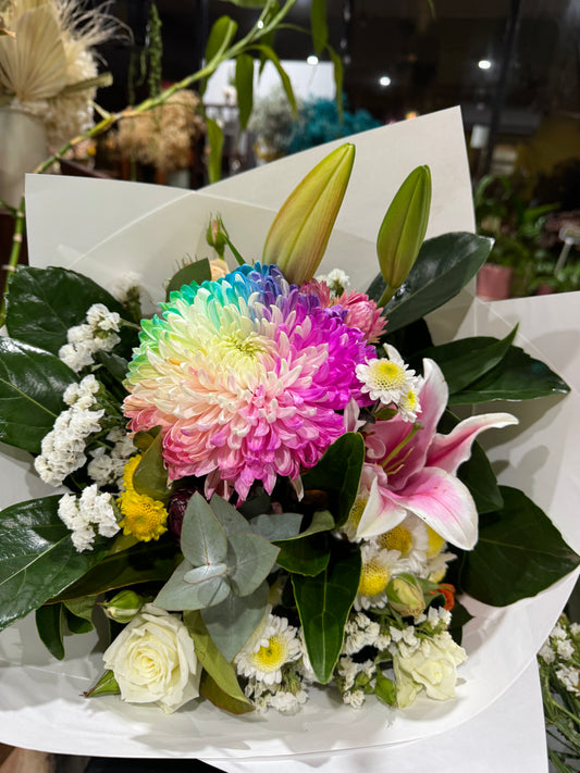 Bouquet of flowers with a colourful flower in the centre, arranged with Oriental lilies, 
statice and daisies with beautiful dark foliage framing the bouquet wrapped in white paper. 